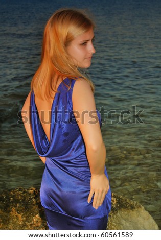 A thoughtful woman in violet dress standing on a small rock on beach