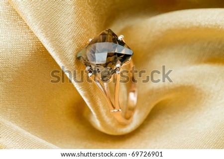 Elegant jewelry ring with jewel topaz  on a background of golden silk