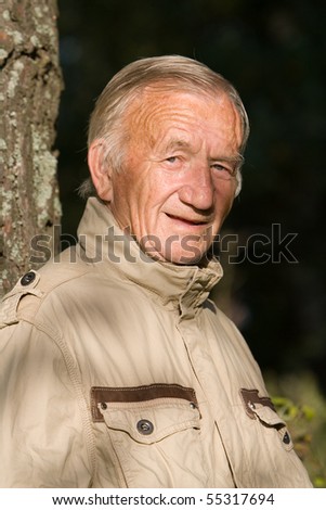 Portrait of the elderly man in a beige jacket in village on the nature