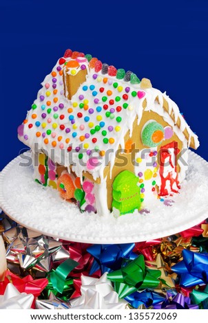 Christmas gingerbread house with sprinkles, gum drops, and other candies. Sits on a cake stand with festive ribbons around the base.