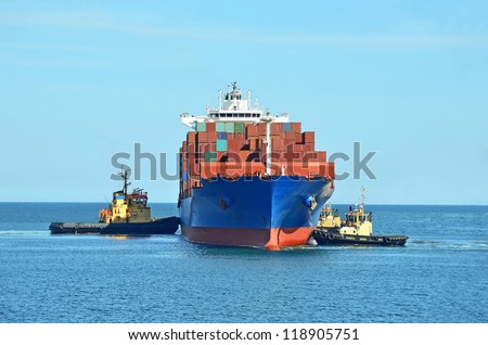 Tugboat assisting container cargo ship to harbor quayside