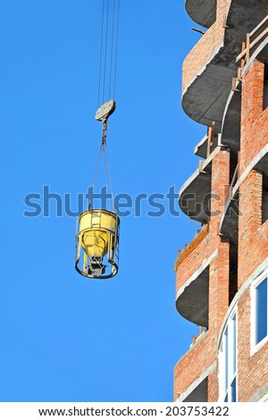 Mobile crane lifting concrete mixer container against blue sky