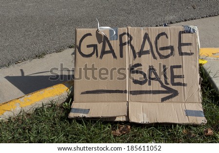 Garage sale text with arrow written on cardboard and placed on grass next to the street