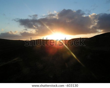Sunset behind hills with sun flare.