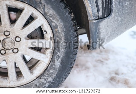 dirty car wheel stands on winter snowy road