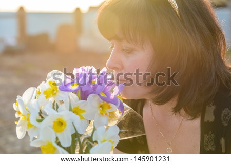 middle-aged woman smelling a bouquet of flowers narcissus