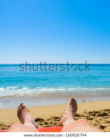 feet of the man lying on a deck chair against the sea
