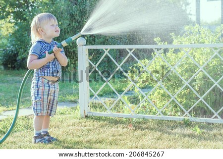 little blond boy pours water from a hose in the garden plant