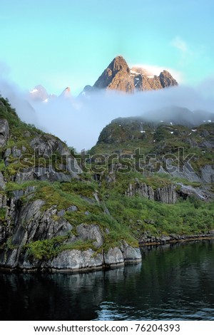 Rocky shore of a Norwegian fjord and a hill surrounded by fog