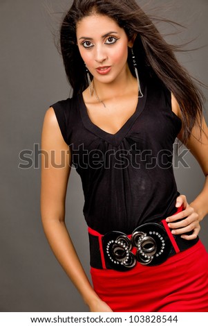 Hot young brunette in red skirt and black blouse against grey background