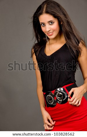 Hot young brunette in red skirt and black blouse against grey background