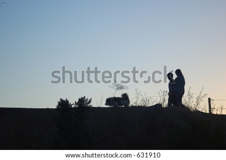 Silhouette of a couple going out for an evening stroll walking their dog.