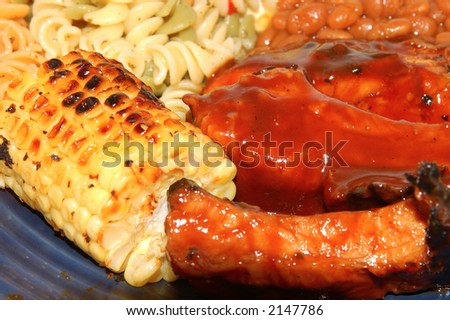spare ribs corn potato and pasta salad and baked beans on a dinner plate