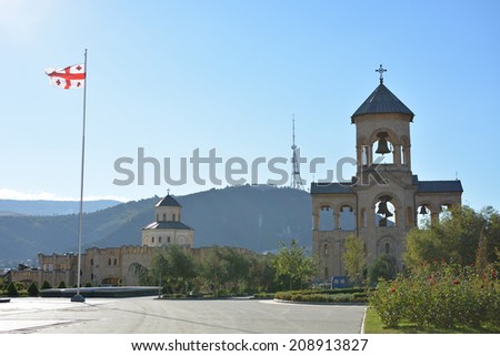 Tbilisi, Georgia - October 7, 2013: Georgian flag fluttering in the wind on the territory of the Holy Trinity Cathedral (Tsminda Sameba), Caucasus Range and TV Tower