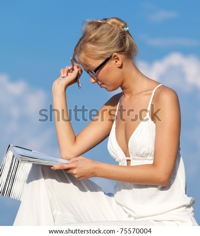The girl wearing spectacles sits on a blue background of the sea and reads