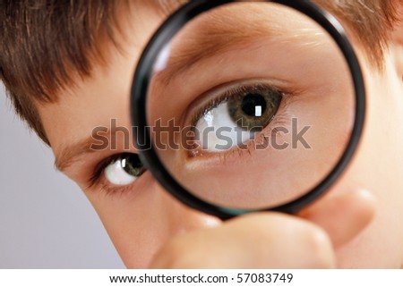close up of a green eyed boy looking through magnifying glass