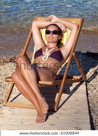 Young woman in dark purple bikini relaxing in a deck chair on sandy beach in Budva, Montenegro