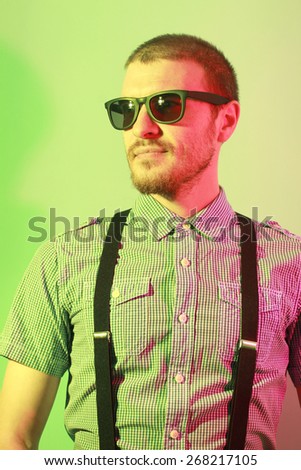 Portrait of handsome casual stylish young man with sunglasses, plaid short sleeve shirt and braces in green and red colored lights