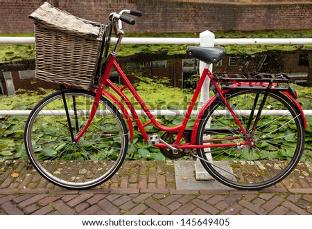 Red bicycle equipped with a large basket, parked beside a water canal in Holland. Riding bicycles is the most popular method of transport in the Netherlands.