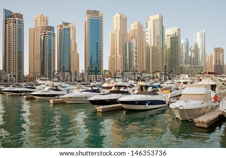 Luxurious Yachts and Boats in Front of Dubai Marina Skyscrapers, in the daylight. All the logos and trade names are removed from the picture.