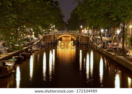 Reflection of illuminated bridges and street lights on the dark water surface of a canal in Amsterdam.