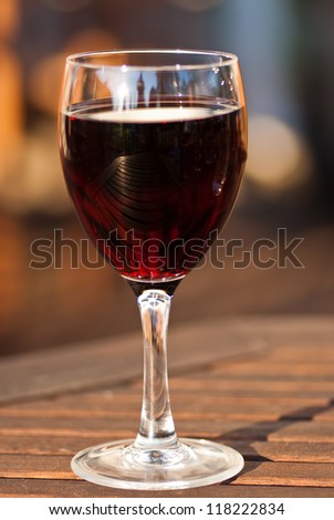 Glass of red wine on table outdoors in evening.