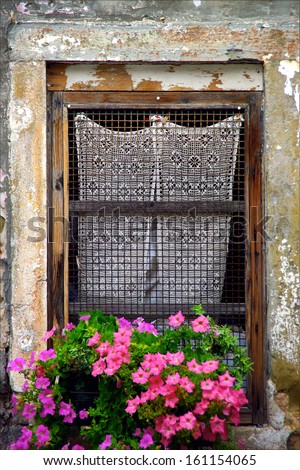 Old window with lace curtain and flower box in summer in Italy.