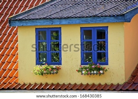 House with loft apartment and two windows with blue frames and window boxes with flowers.
