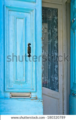 Blue front door with a mail slot and lace curtain inside.