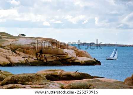 Landscape with ocean and red granite boulders and a sailing boat at the Swedish west coast.