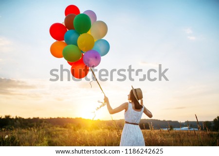 Girl with colorful balloons walking in wheat field