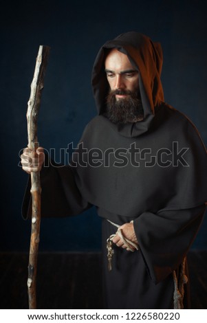 Medieval monk in robe with hood rests on a stick