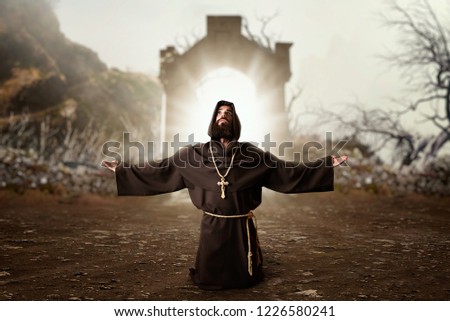 Monk in black robe with hood kneeling and praying