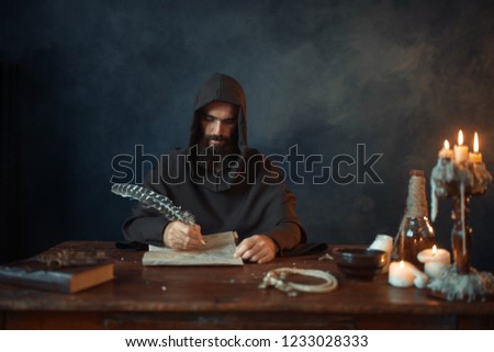 Medieval monk in robe writes with a goose feather