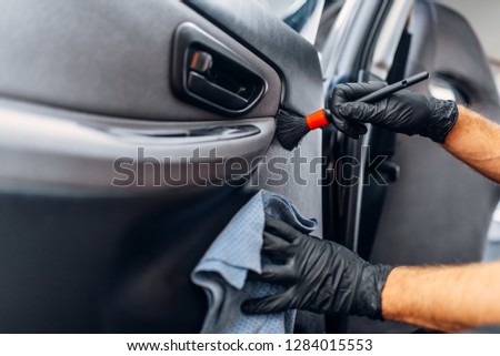 Auto detailing, worker cleans door trim with brush