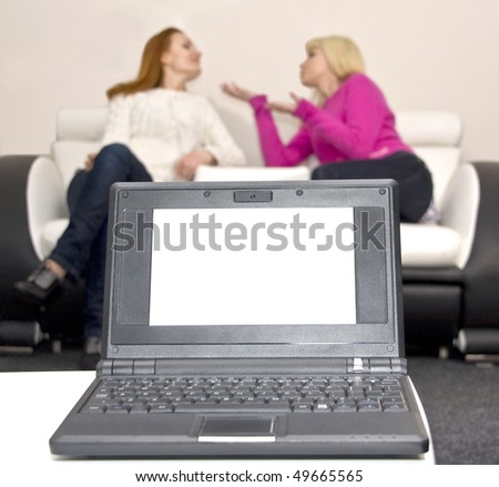 Laptop with blank screen and two talking woman on background