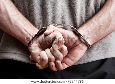 Criminal hands locked in handcuffs. Close-up view