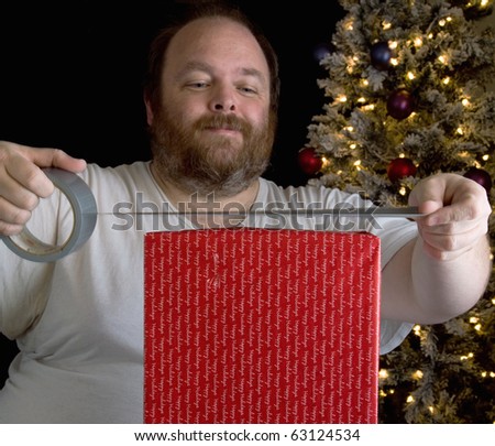 Middle aged man in tee shirt wrapping Christmas present with duct tape.