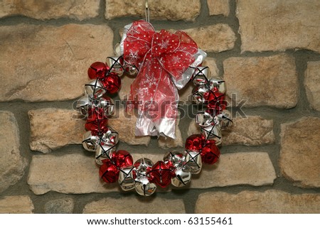 Holiday wreath made from silver and red bells hung on stone wall