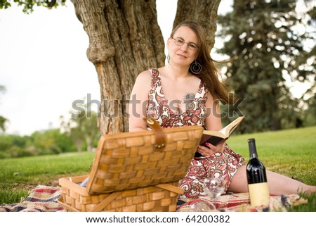 Woman enjoying the summer with a good book, picnic and bottle of wine