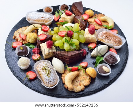 Assorted sweets, lot of sweets, cakes, fruit and chocolate on a slate base. Isolated. The concept for a restaurant.