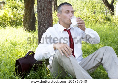 The happy businessman drinks fresh milk in summer solar garden