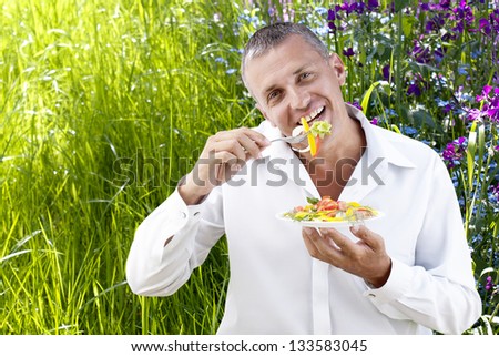 Adult man eating fresh vegetable salad on a summer nature background