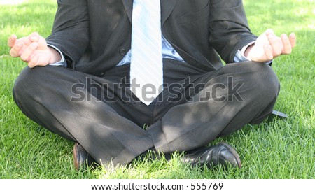 Young man in business suit and tie sits on green lawn and meditates on company time