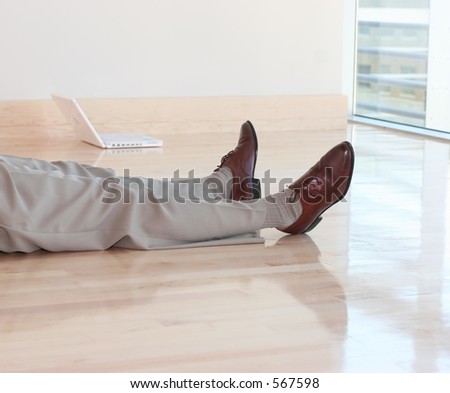 Businessman rests on wooden floor with no furniture with small, wireless laptop and window in background