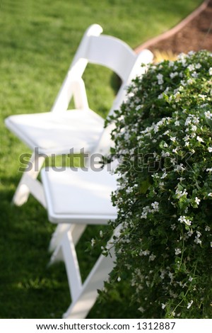 Two white lawn chairs sitting in the grass next to flowers