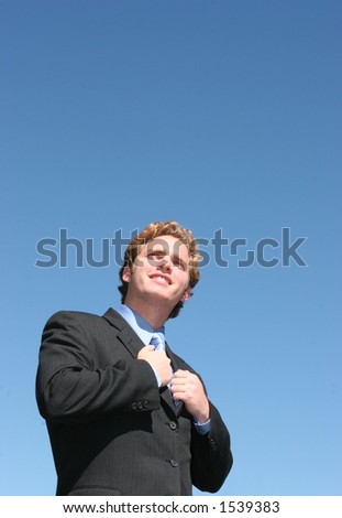 Business man in black suit and blue shirt holding onto the inside of his suit, looking up