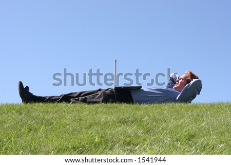 Business man on his back enjoying the laptop in the green grass across the blue sky