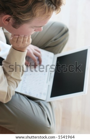 Business man in tan shirt is looking down to his laptop on his lap on wooden floors