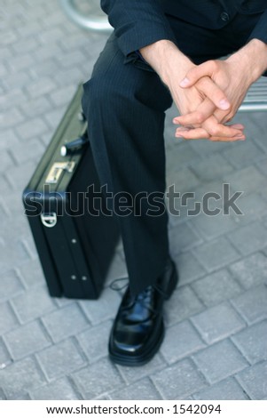 Business man is sitting down next to briefcase holding his hands
